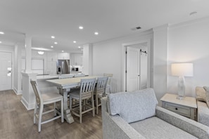 A modern kitchen with white cabinetry, a dining area with a table and chairs, and a living area with a sofa and a lamp.