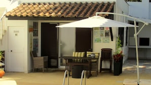 Un espace piscine avec une table et des chaises, un parasol blanc et une porte portant l’inscription « WC ».