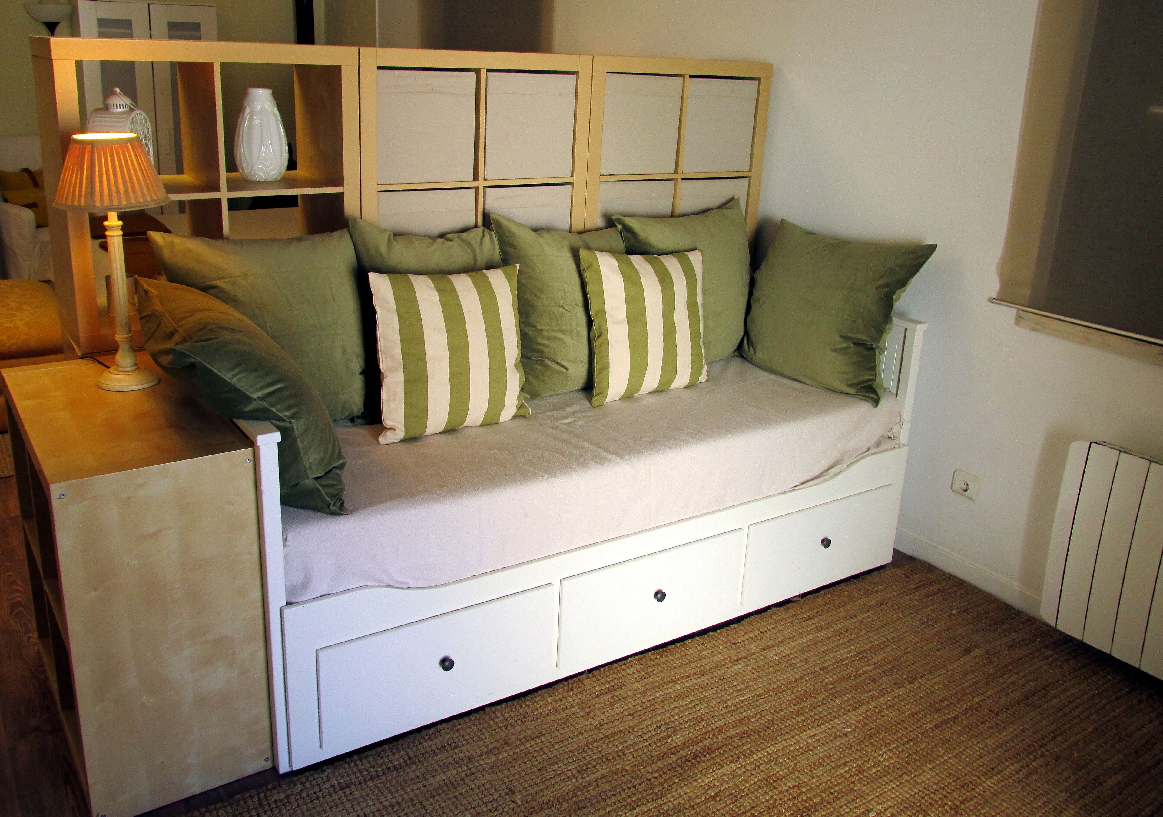 Habitación individual con una cama y cabecera de madera, una mesita de noche con lámpara y un radiador.