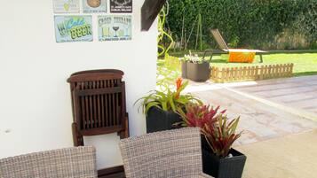 An outdoor seating area with wicker furniture, a table with a decorative bowl, and a wall with various beverage-related posters.