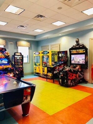A room with arcade games, a pool table, and a large screen displaying a game. - Luxury 7 Bdr~Private Pool at Champions Gate (Four Corners)