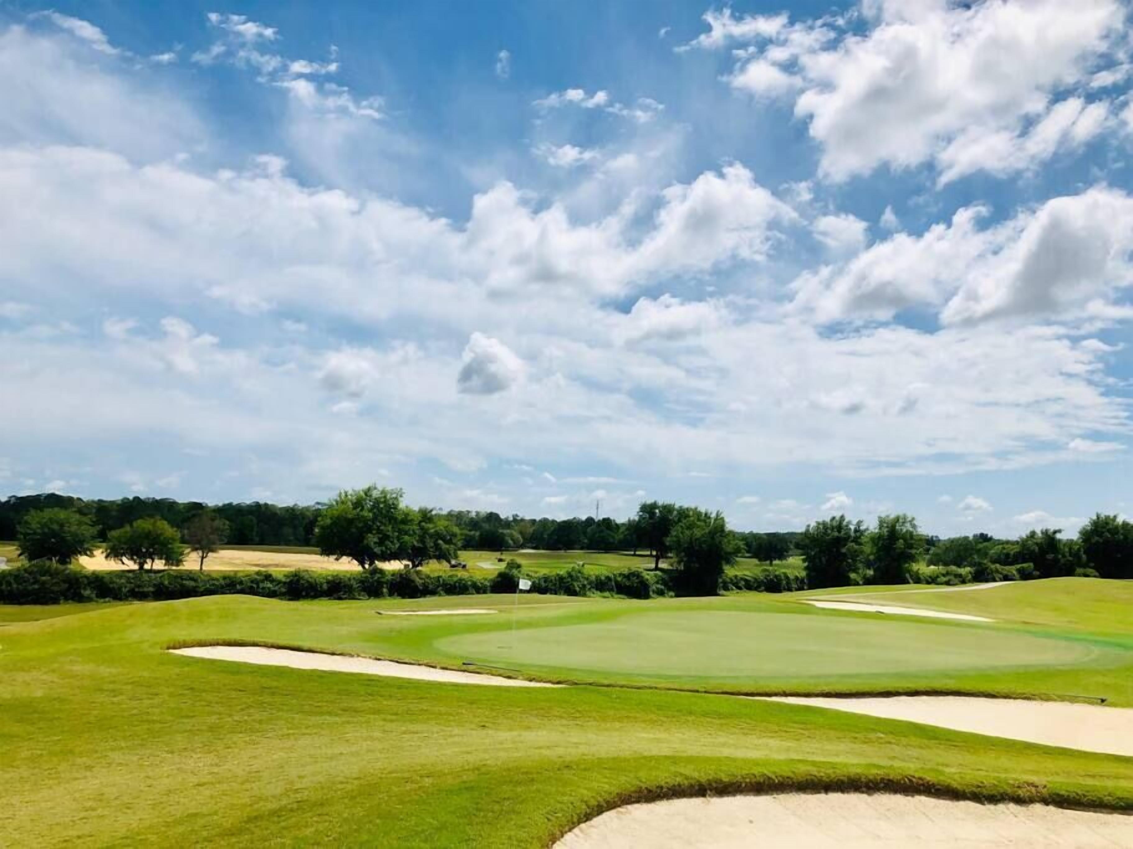 A golf course with sand bunkers, well-maintained grass, and a clear blue sky.
