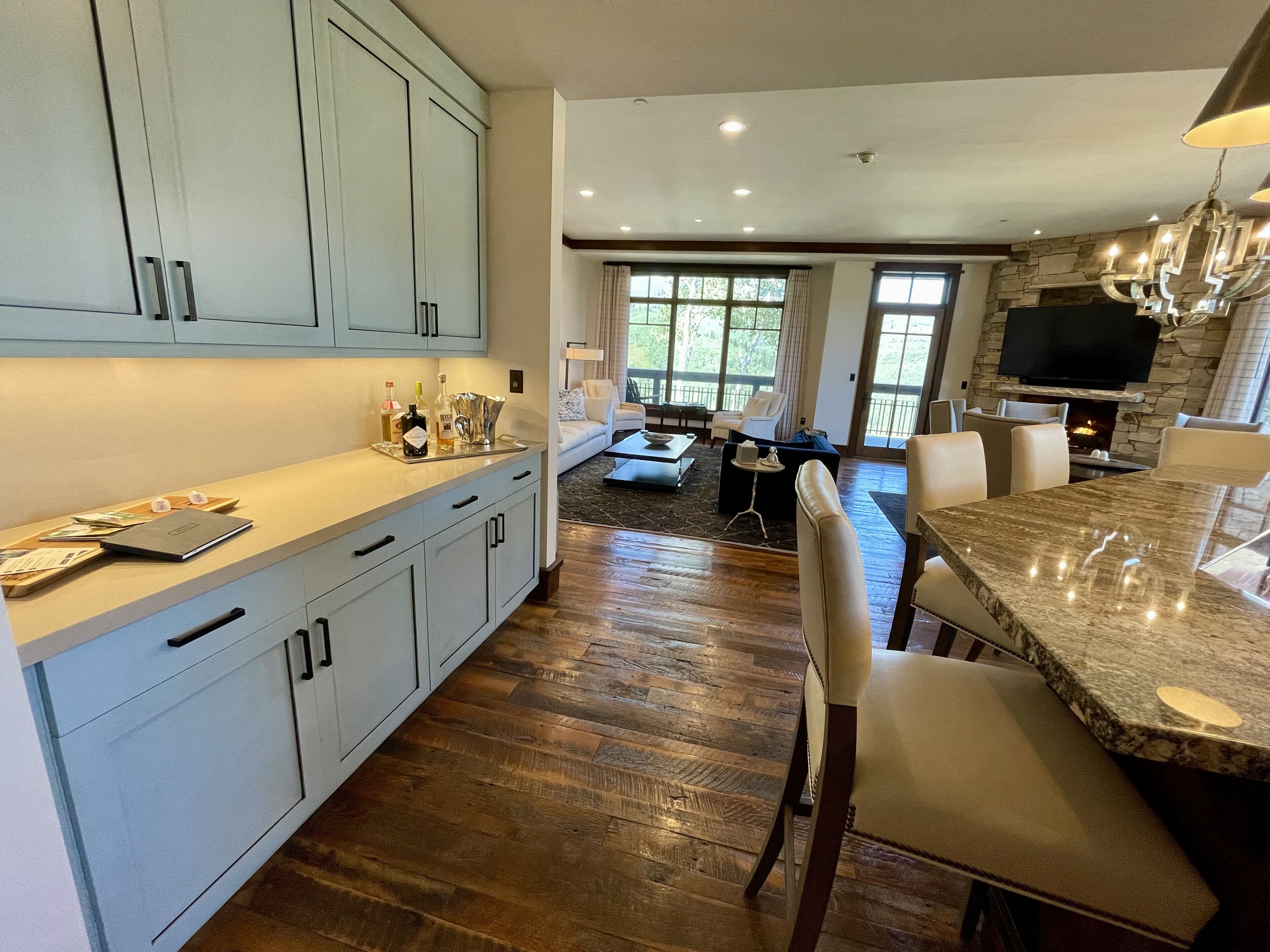 A modern kitchen with light blue cabinets, a marble countertop, and a dining area with leather chairs.