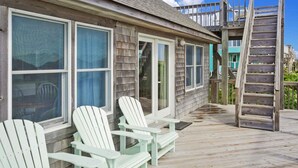 A wooden deck with Adirondack chairs, a wooden ladder, and a house with large windows and a balcony. - Oceanfront Cottage with Grill, Deck, and Beach Only Steps Away. It's No Problem! (Avon)