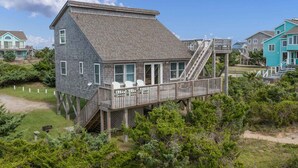 A wooden house with a steep roof, a deck, and a staircase leading to a second level. - Oceanfront Cottage with Grill, Deck, and Beach Only Steps Away. It's No Problem! (Avon)
