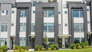 Un moderno edificio residencial de varios pisos, con fachada simétrica, ventanas grandes y un césped bien cuidado con flores amarillas.