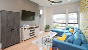 Una sala de estar moderna con un armario gris, un televisor de pantalla plana, un conjunto de sofá azul y un ventilador de techo.