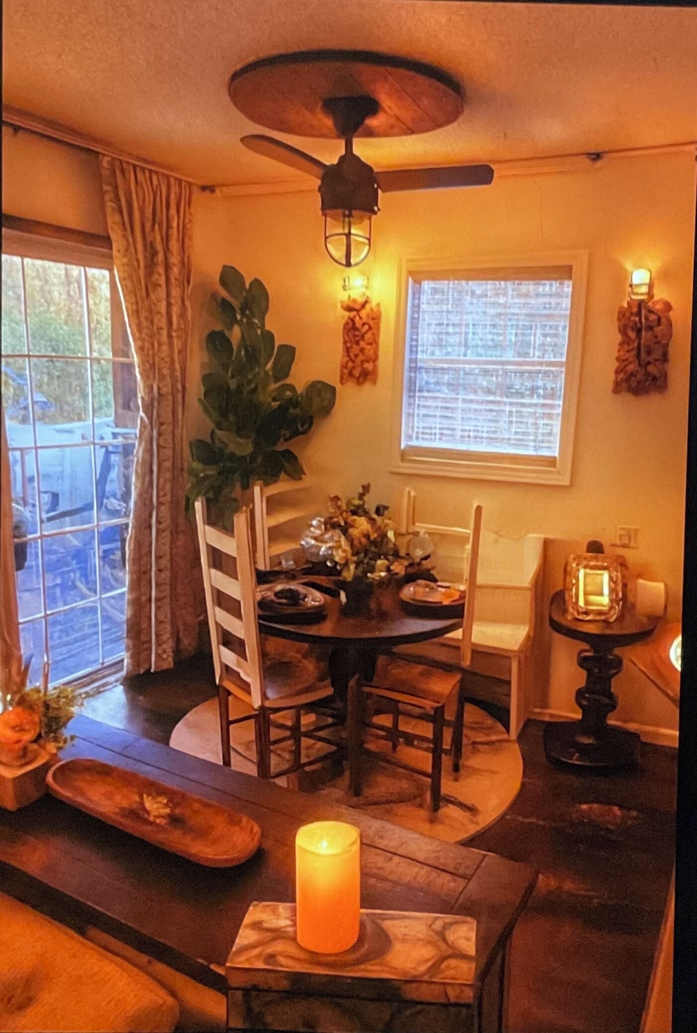 Un coin repas chaleureux avec une table ronde, des chaises, une bougie et un ventilateur de plafond.