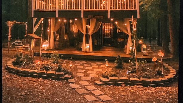 Een houten huis met twee verdiepingen, een balkon, lichtslingers en een parasol.