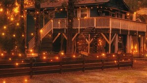 Een houten huis met veranda en wenteltrap, omringd door lichtslingers.