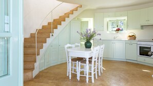 A kitchen with white cabinets, a dining table with chairs, a stove, and a staircase.