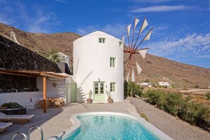 Un bâtiment blanc avec un moulin à vent, une piscine et un mur en pierre.