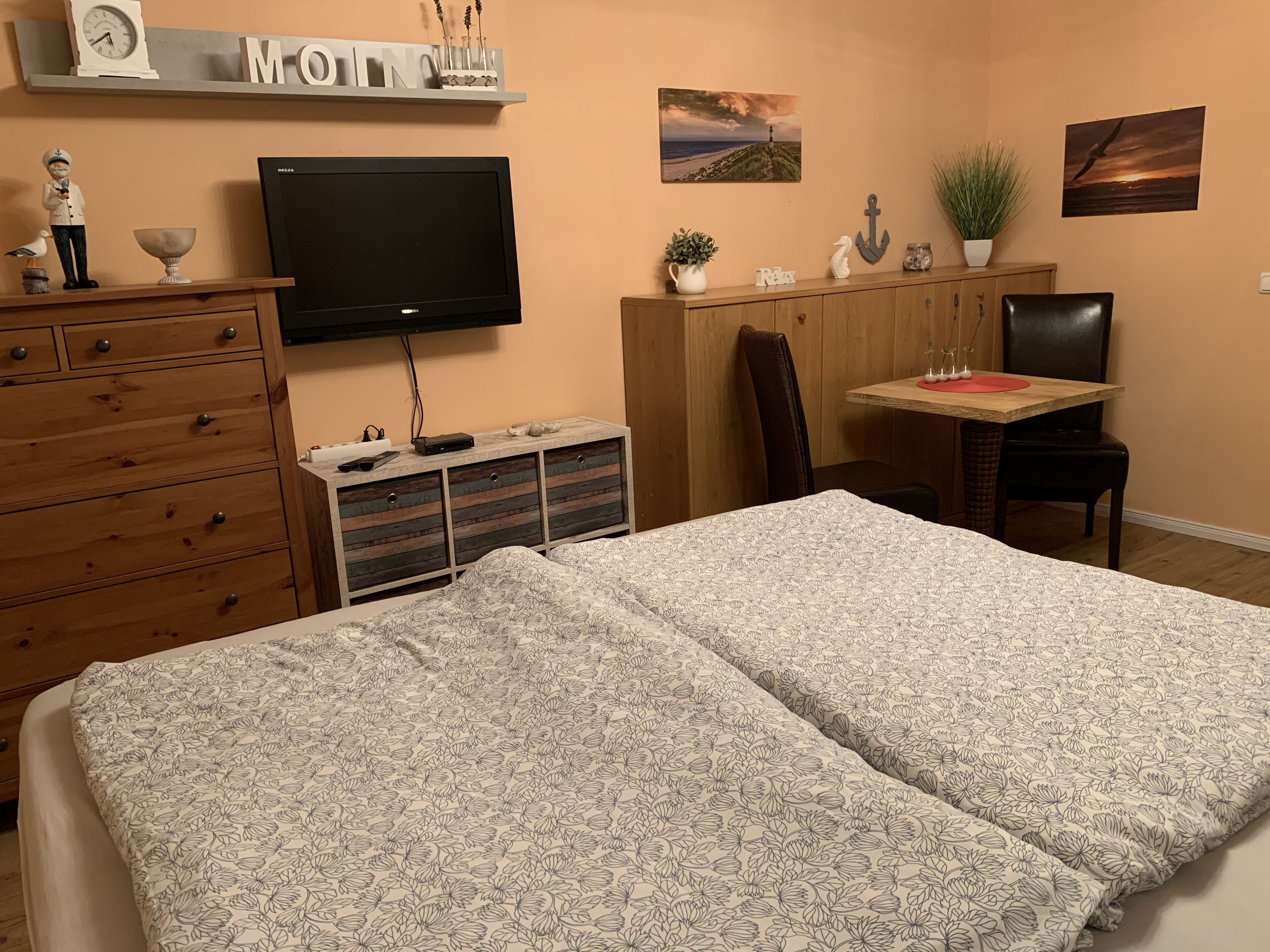 Een slaapkamer met een bed, een dressoir, een televisie, bureau, stoel en kunstwerken aan de wanden.