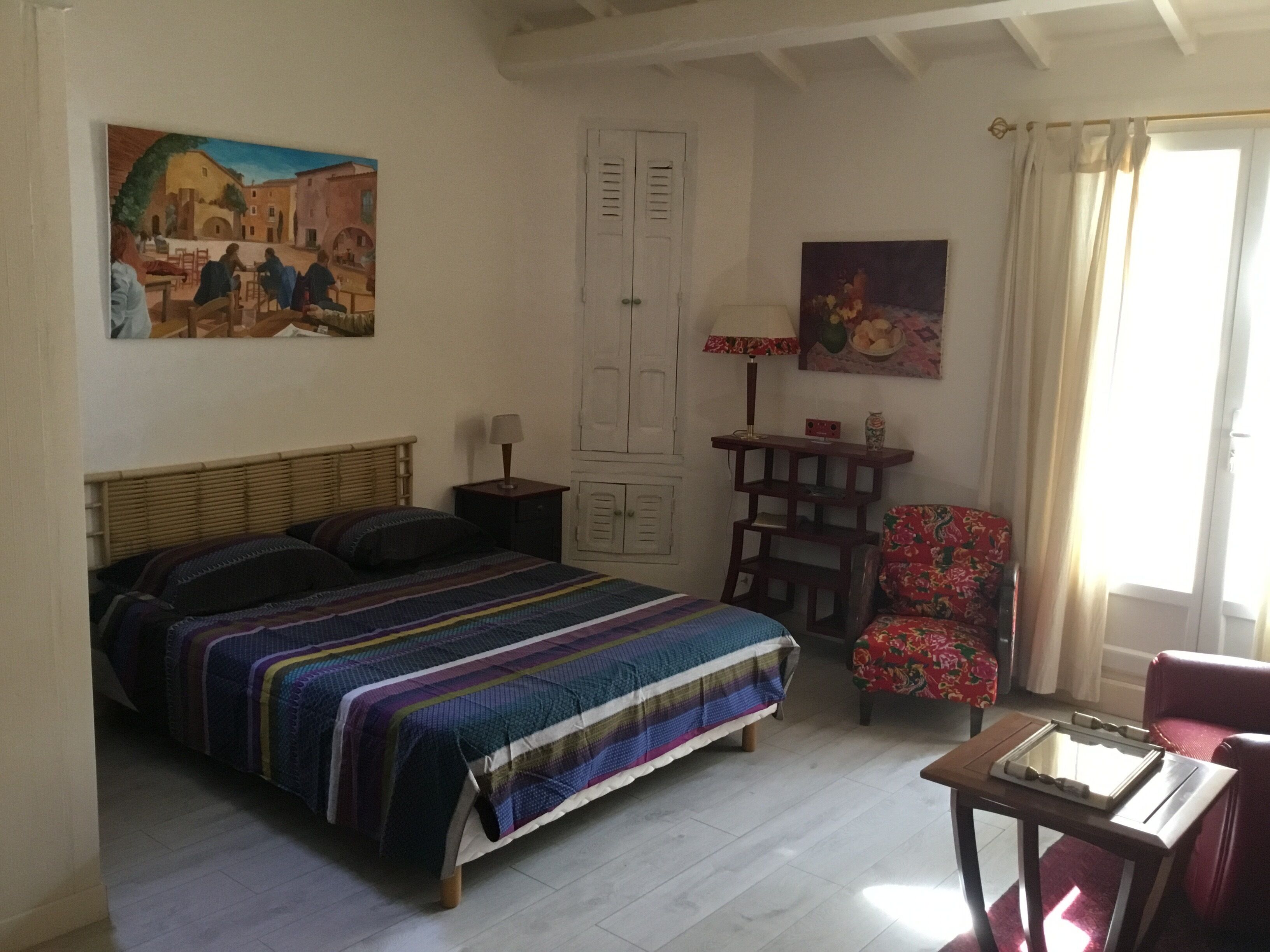 A bedroom with a bed, a chair, a table, and two paintings on the walls.