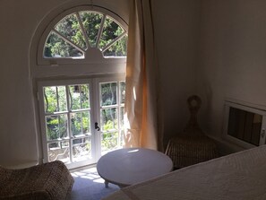 A room with a large arched window, a round table, and a wicker chair.