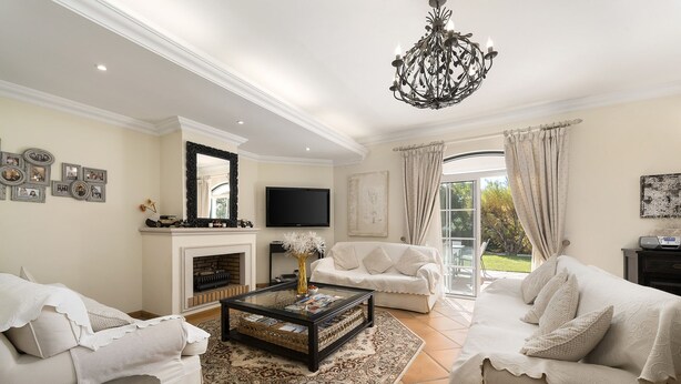 A spacious living room with a fireplace, two white sofas, a coffee table, and a chandelier. - Semi-detached house, 500m from the lake in Quinta do Lago, perfect for your vacation (Almancil)