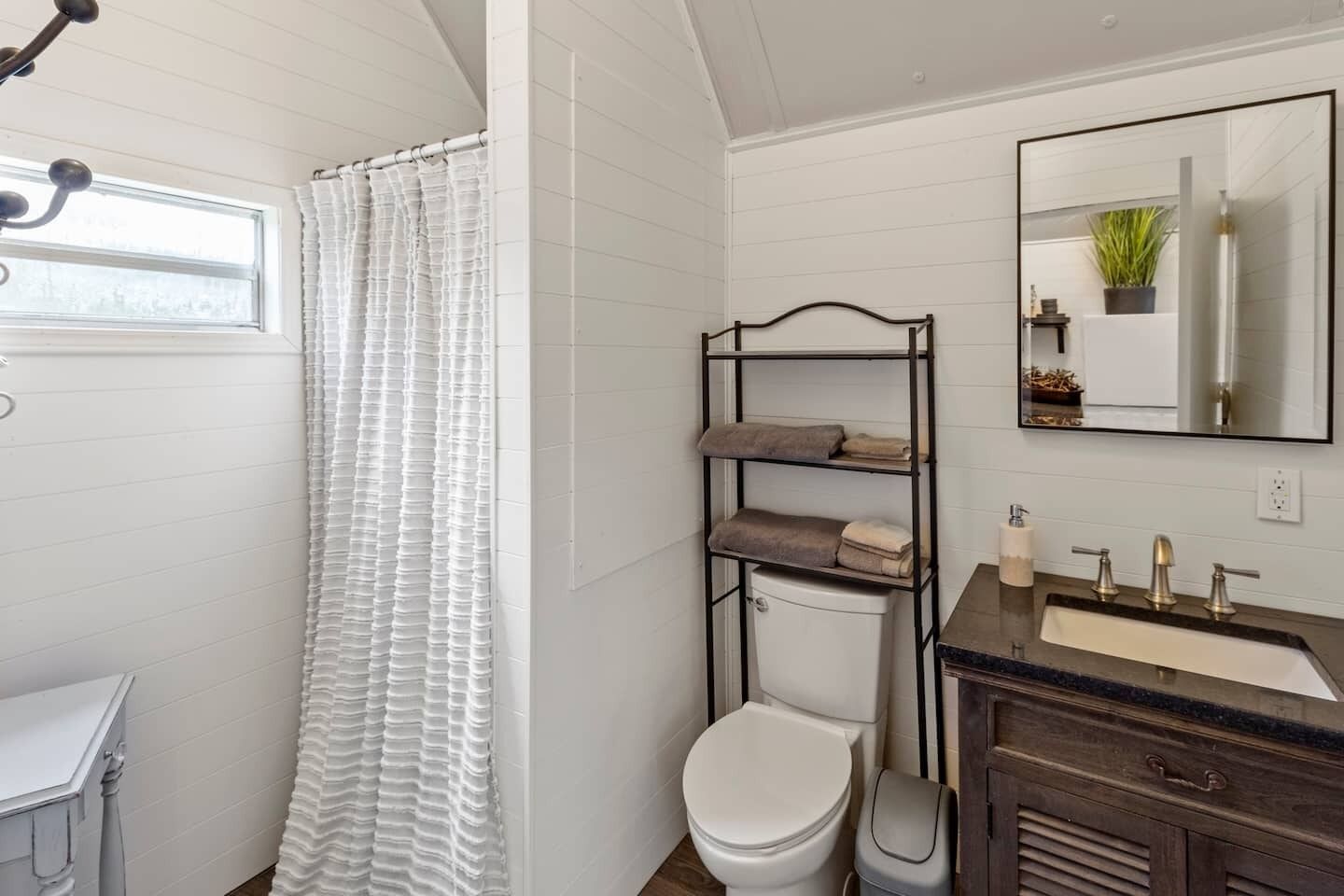 A bathroom with a white toilet, a sink with a mirror above it, and a shelf unit with towels.