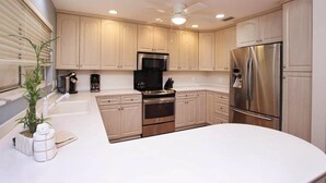 A modern kitchen with light wood cabinets, stainless steel appliances, and a white countertop. - Sandcastle Home (Sanibel)