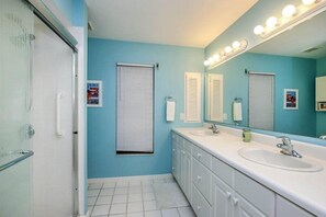 A bathroom with two sinks, a large mirror with lights, and a shower area. - Sandcastle Home (Sanibel)