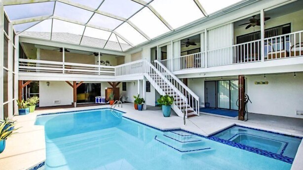 An indoor swimming pool with a glass ceiling, multiple balconies, and a staircase. - Sandcastle Home (Sanibel)