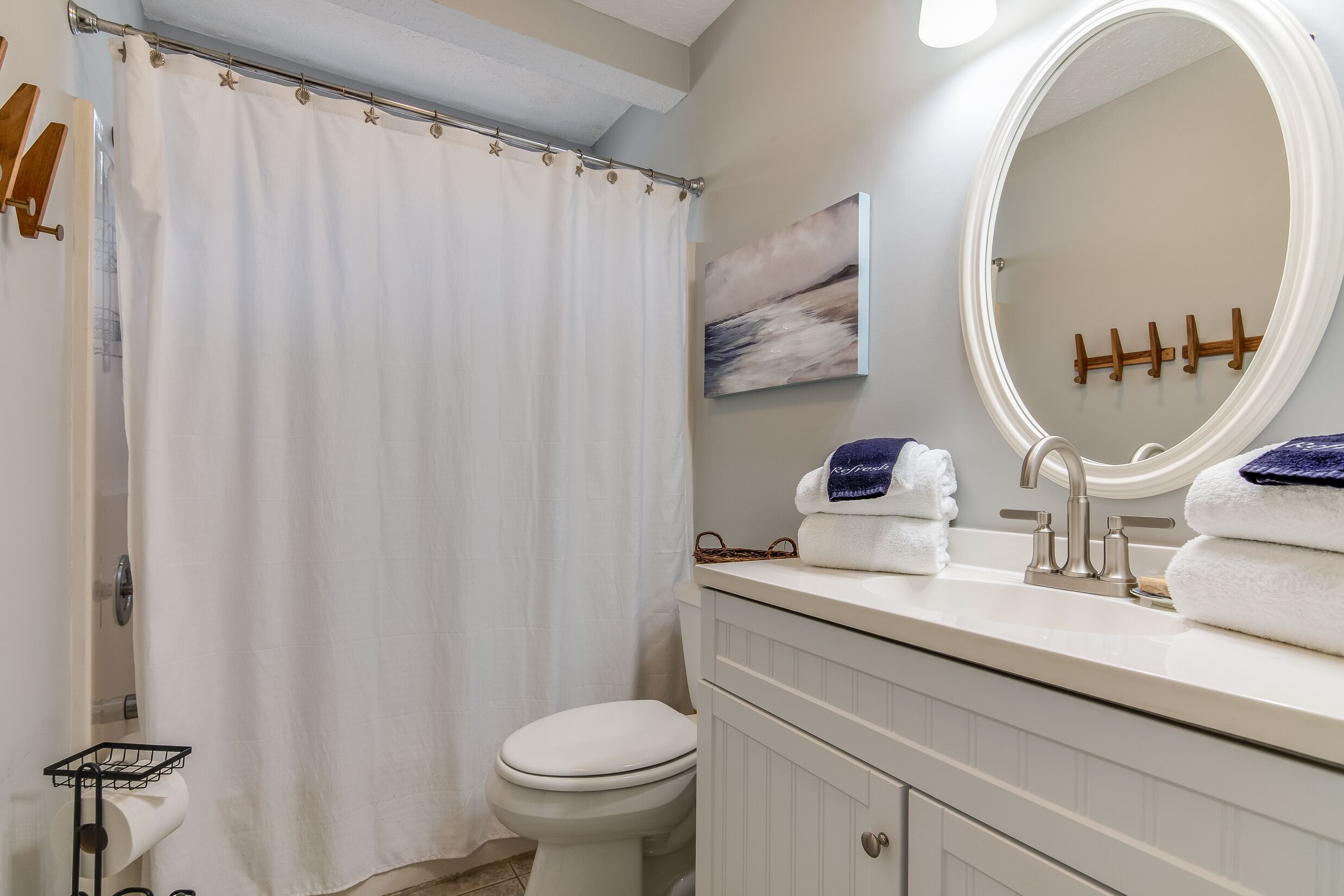 A bathroom with a toilet, a sink with a mirror, a shower curtain, and towels on the sink.