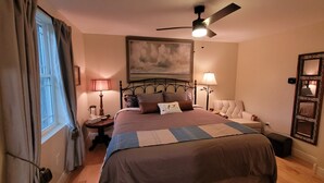 A bedroom with a bed, a ceiling fan, a nightstand, a chair, and a painting on the wall.