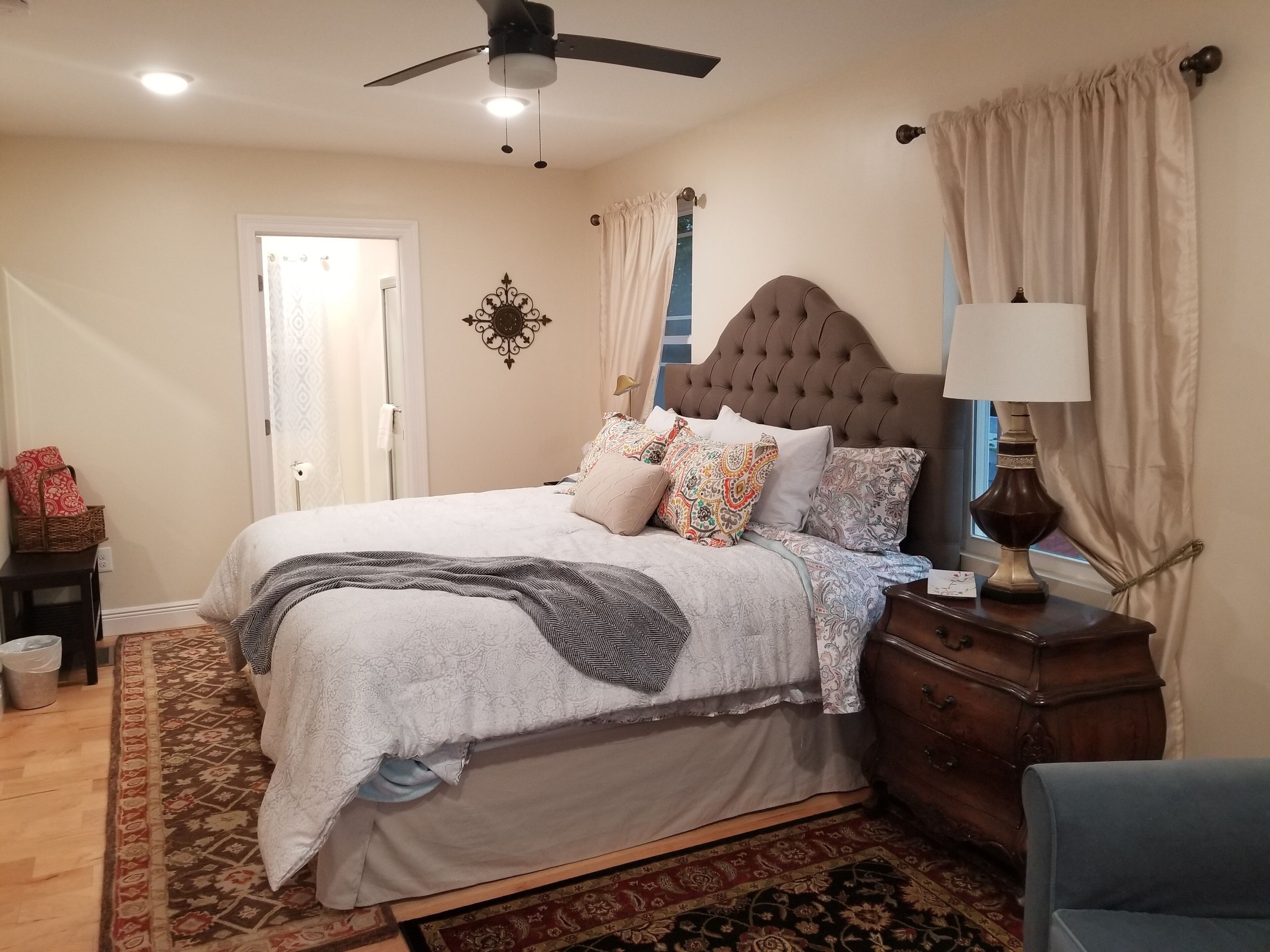 A bedroom with a tufted headboard, a bed with patterned bedding, a bedside lamp, a wooden nightstand, and a patterned rug.