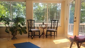 A room with a large window, wooden flooring, a blue exercise mat, two chairs, a small table, and a potted plant.