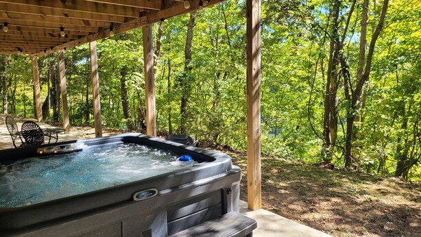 A hot tub under a wooden pergola surrounded by a forest.