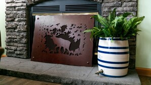 Una chimenea con un panel metálico decorativo que muestra un diseño de ciervo y follaje, integrado en una pared de piedra.