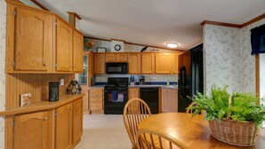 Una cocina con armarios de madera, microondas, estufa y refrigerador. Hay una mesa de comedor con sillas y una cesta con plantas verdes.