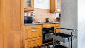 Eine Küche mit Holzschränken, einer Mikrowelle, einem Backofen und einem schwarzen Tablettregal.