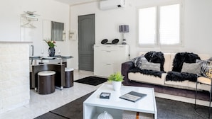 Ein modernes Wohnzimmer mit einem Glastisch, einer Couch mit schwarz-weißen Kissen, einem Essbereich mit einem Glastisch und Stühlen sowie einer Küche mit einem weißen Kühlschrank und Schränken.