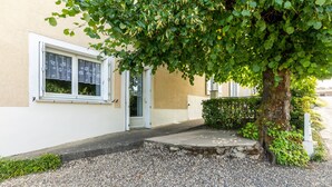 Un edificio con camino de grava, un árbol frente a él y una puerta blanca.