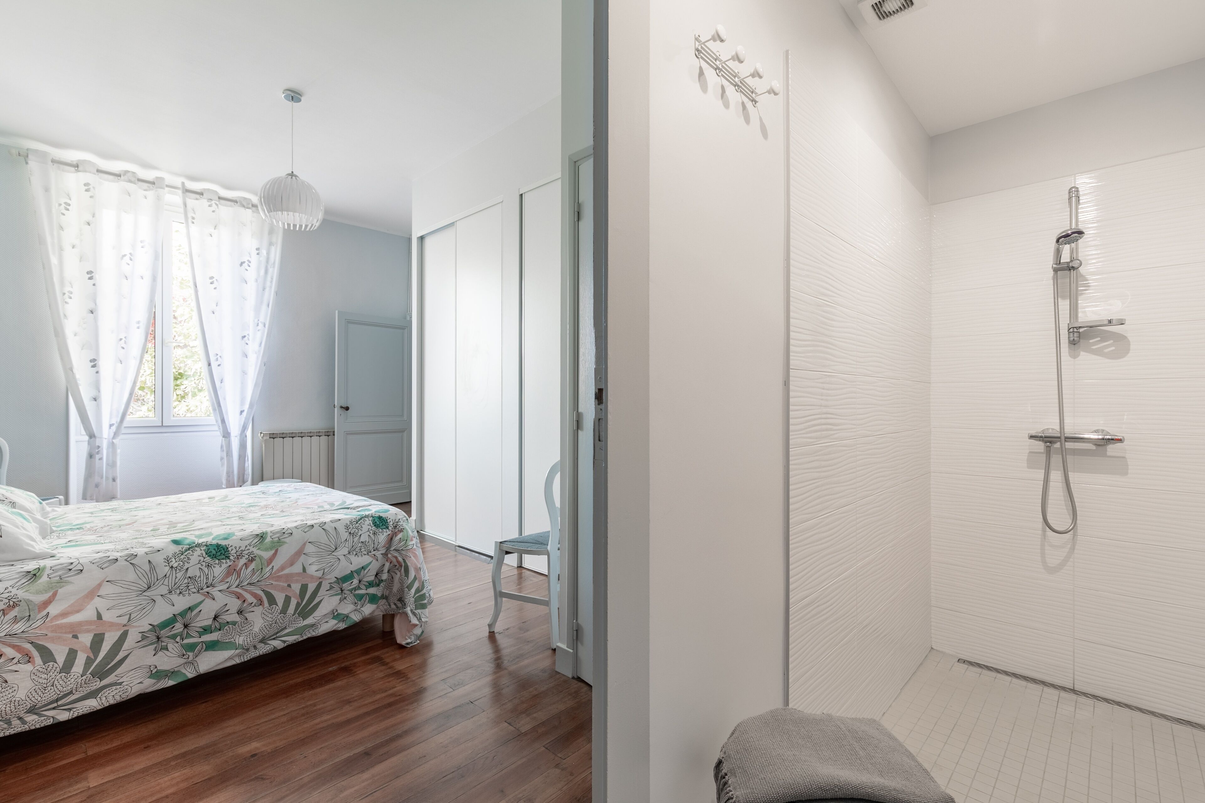 Ein Schlafzimmer mit einem Bett, einem Sessel, einer Dusche und einem Fenster mit Vorhängen.