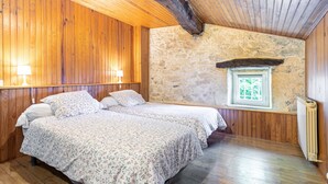 Una habitación con paredes de madera, una pared de piedra, una ventana y una cama con ropa de cama estampada.