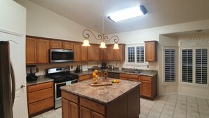 A kitchen with wooden cabinets, a granite countertop, a stainless steel oven, a microwave, and a pendant light fixture. - Rancho Encantado VIP (El Paso)