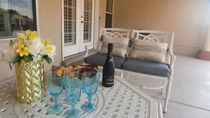 A table with a vase of flowers, a bottle of champagne, and fruit on a white metal table. - Rancho Encantado VIP (El Paso)