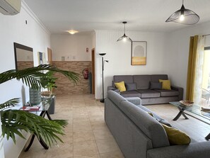 Una sala de estar moderna con un sofá gris, una mesa de centro de vidrio y una planta grande.