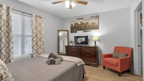 Une chambre à coucher comprenant un lit, une commode, une chaise, un ventilateur de plafond et un téléviseur.