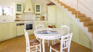 A kitchen with a round table, white chairs, a stove, and a staircase.