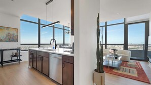 Eine moderne Küche mit einer großen Kochinsel, ein Essbereich mit einer Couch und große Fenster mit Blick auf die Stadt.