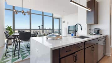 A modern kitchen with a large island, a dining area with a view, and a cityscape visible through large windows.