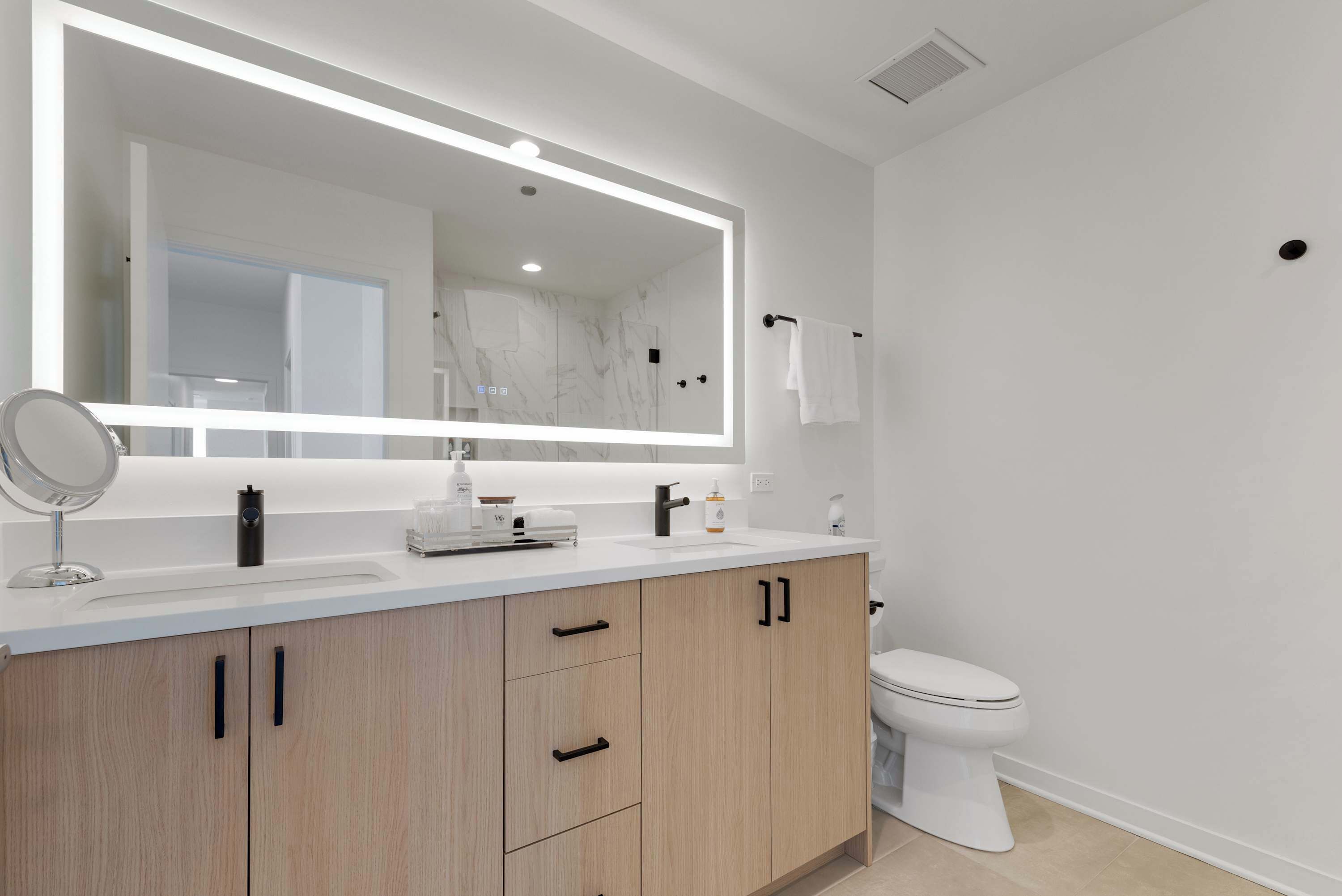 A modern bathroom with a white vanity, a large mirror, and a toilet.