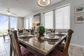 Une salle à manger avec une table en verre, des chaises en osier et une vue sur l’extérieur.