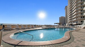 Une piscine avec un soleil dans le ciel, des chaises longues et un immeuble de grande hauteur en arrière-plan.