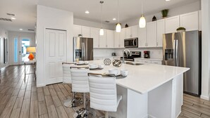Una cocina moderna con armarios blancos, electrodomésticos de acero inoxidable y una isla central con taburetes de bar.