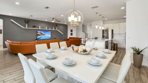 Una cocina moderna con armarios blancos, un refrigerador de acero inoxidable y una zona de comedor con una mesa blanca dispuesta para seis personas.