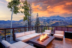 Una terraza con fogata, asientos al aire libre y vistas a la montaña.