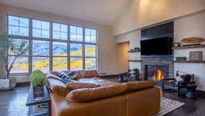 Un salon moderne doté d’une grande fenêtre, d’un canapé en cuir, d’un téléviseur à écran plat, d’une cheminée et offrant une vue sur les montagnes.